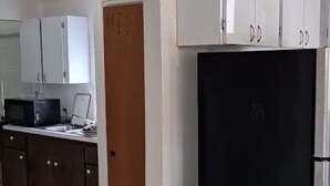 Una cocina con armarios blancos, un refrigerador negro y una puerta de madera.