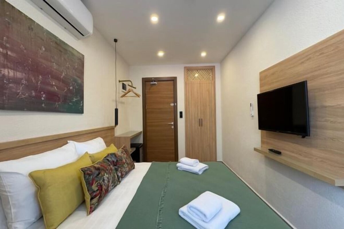 A hotel room with a bed, a TV, a wooden door, and a painting on the wall.