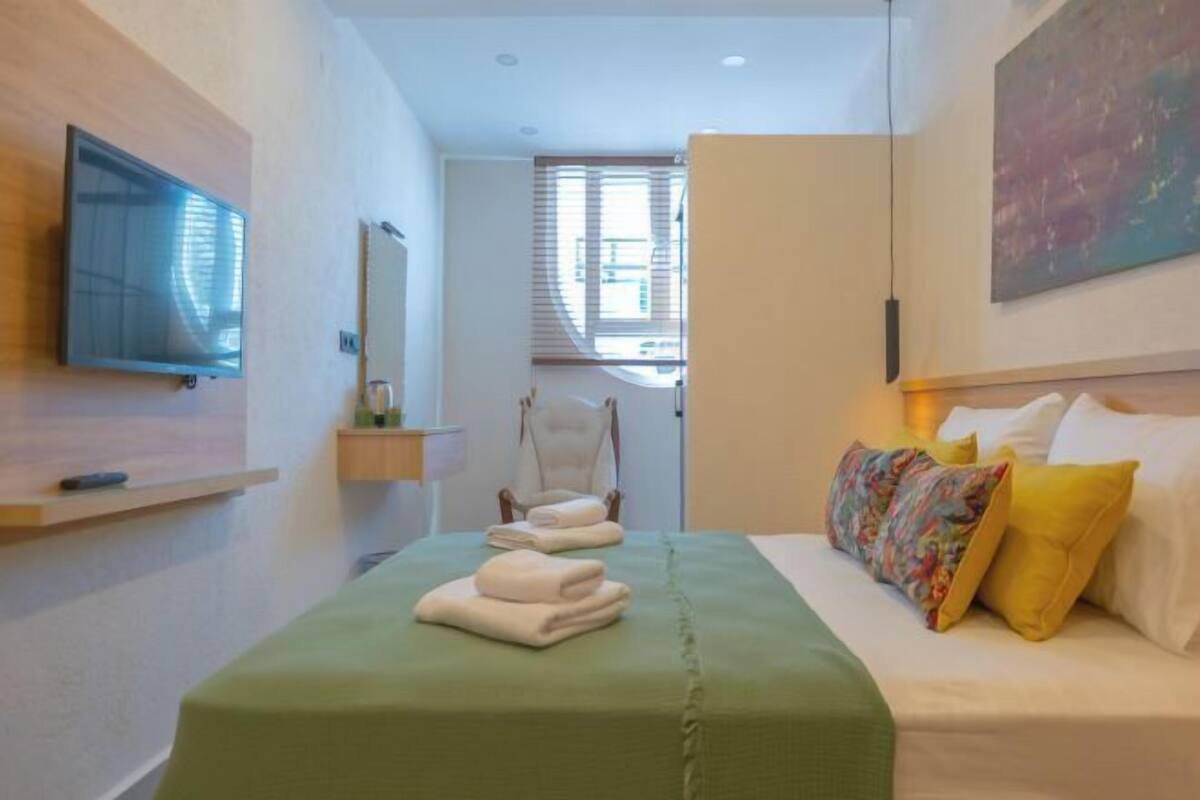 A hotel room with a bed, a chair, a TV, and a window.