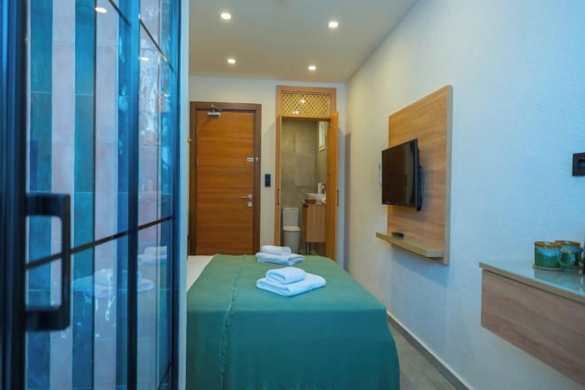 A hotel room with a bed, a TV mounted on the wall, and a bathroom visible through an open door.