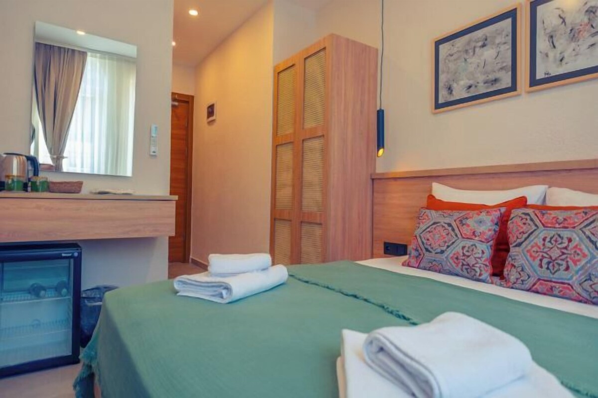 A hotel room with a bed, a desk with a computer, a wardrobe, and a small refrigerator.