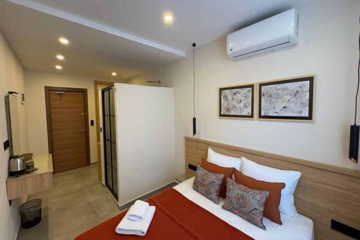 A hotel room with a bed, a wall-mounted air conditioner, and two framed pictures.