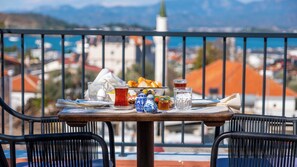 A table with a meal set, including a plate of food, a glass of tea, and a jug of honey, on a balcony with a view of buildings and mountains. - Uva Rooms (Fethiye)