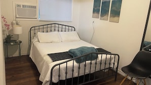 Ein Schlafzimmer mit einem Bett, einem Nachttisch mit Lampe, einem Sessel und einem Fenster mit Jalousien.