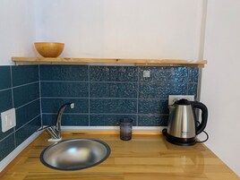 Una cocina compacta con un lavamanos, una tetera y un bol en un estante.