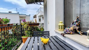 En balkon med en træbænk, et gult pynteting og en farverig skulptur.