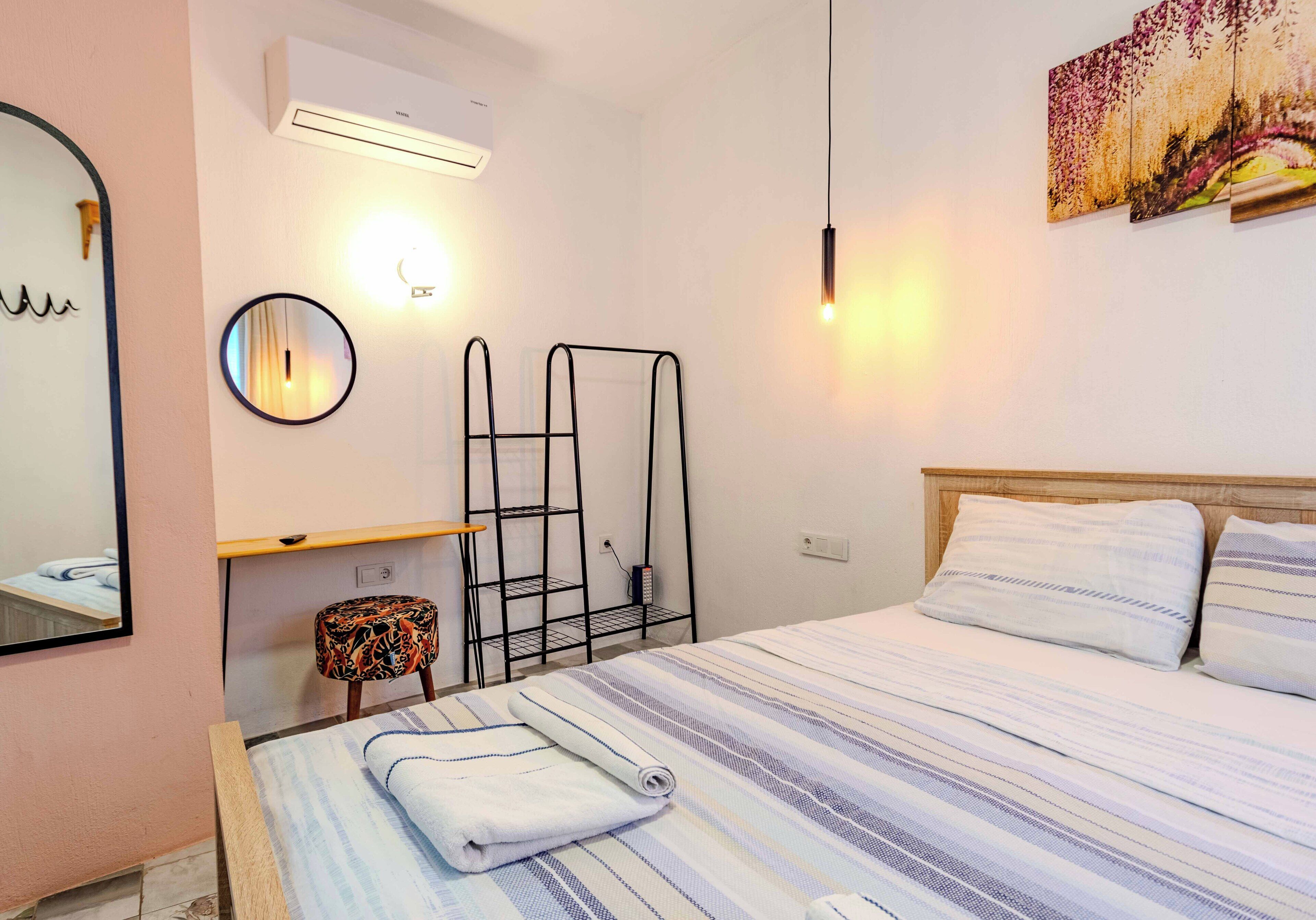 A hotel room with a bed, a bedside table, a mirror, a radiator, and a wall-mounted air conditioner.
