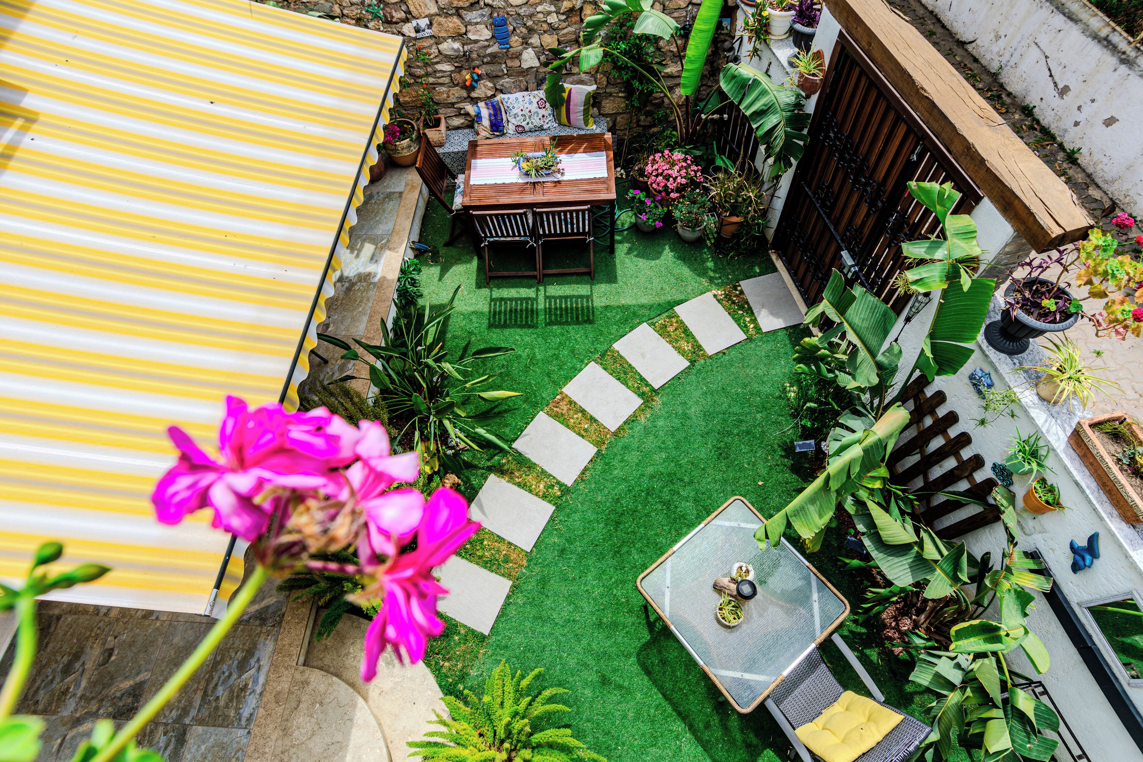 Une terrasse avec une table et des chaises, entourée de plantes en pot et d’un petit jardin.