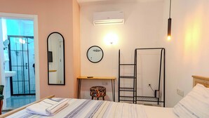 Et hotelværelse med en seng, et lille bord, en stol, et spejl, en fastgjort aircondition og et vindue med udsigt til en pool.
