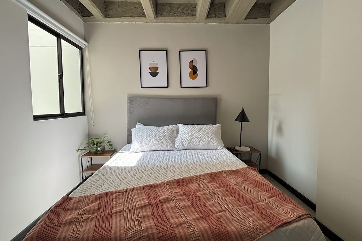A bedroom with a bed, a nightstand, a lamp, and two framed pictures on the wall.