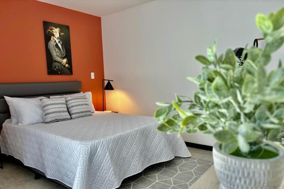 A bedroom with a bed, a nightstand, a lamp, and a potted plant.