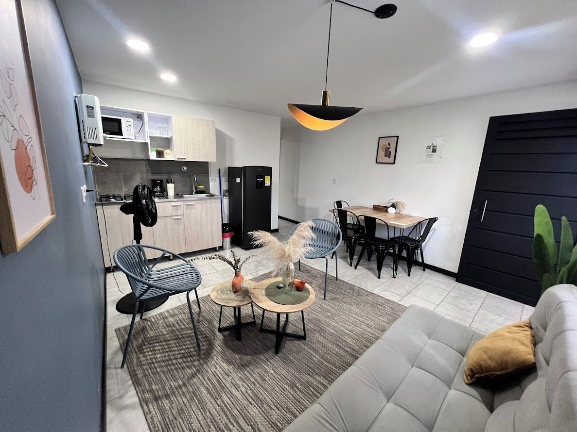 A modern kitchen with a microwave, stove, and refrigerator. There is a dining area with a table and chairs, and a living room with a sofa and a coffee table.