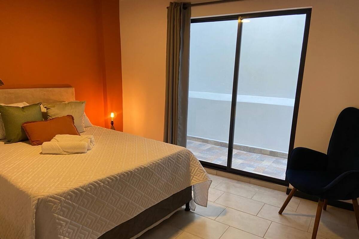 A hotel room with a bed, a chair, and a large window with a view.