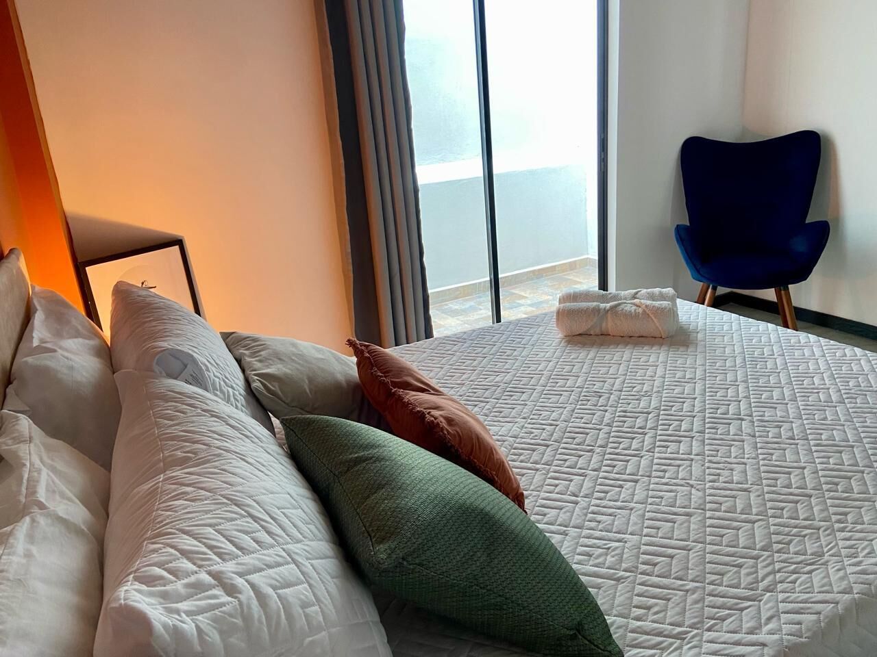 A hotel room with a large bed, a blue chair, and a view of the sea through a large window.