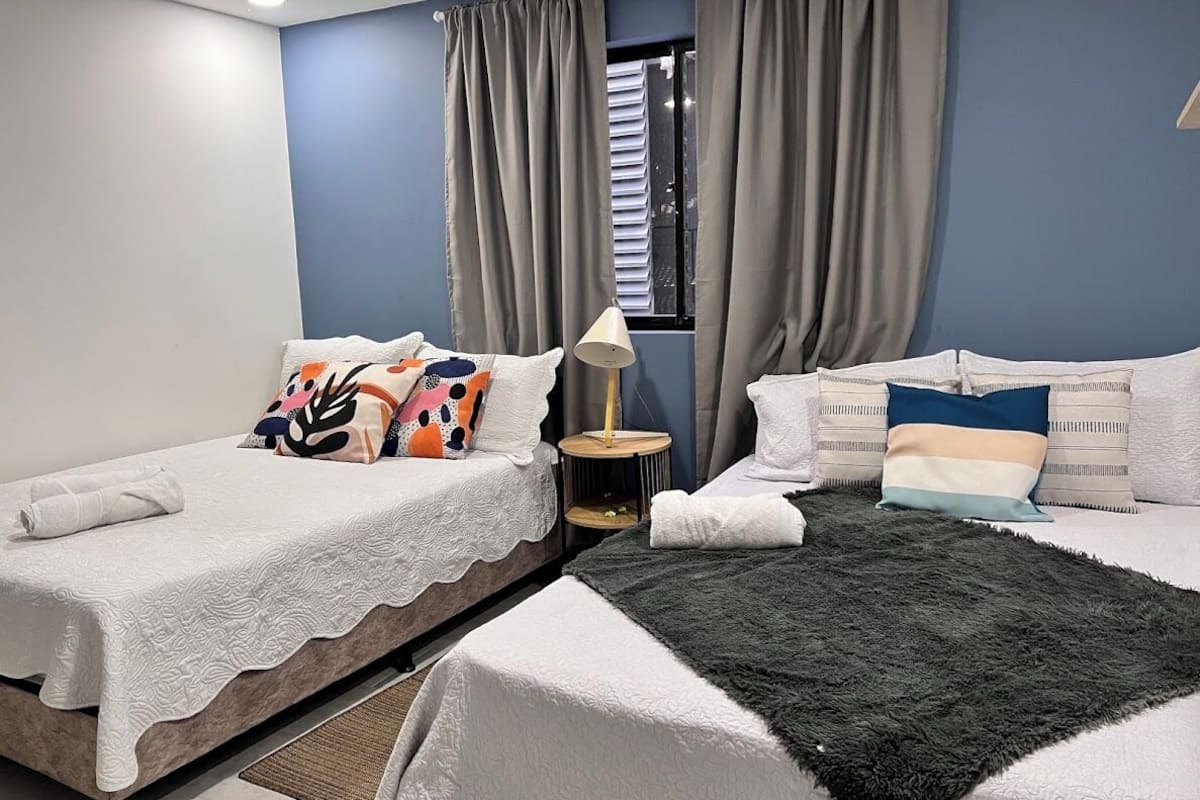A bedroom with two beds, a window with curtains, a lamp, and a small table.