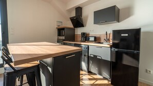 A modern kitchen with a wooden dining table, black appliances, and a microwave. - Charming apartment 200m from ocean with terrace and parking (Mimizan-Mimizan Plage)
