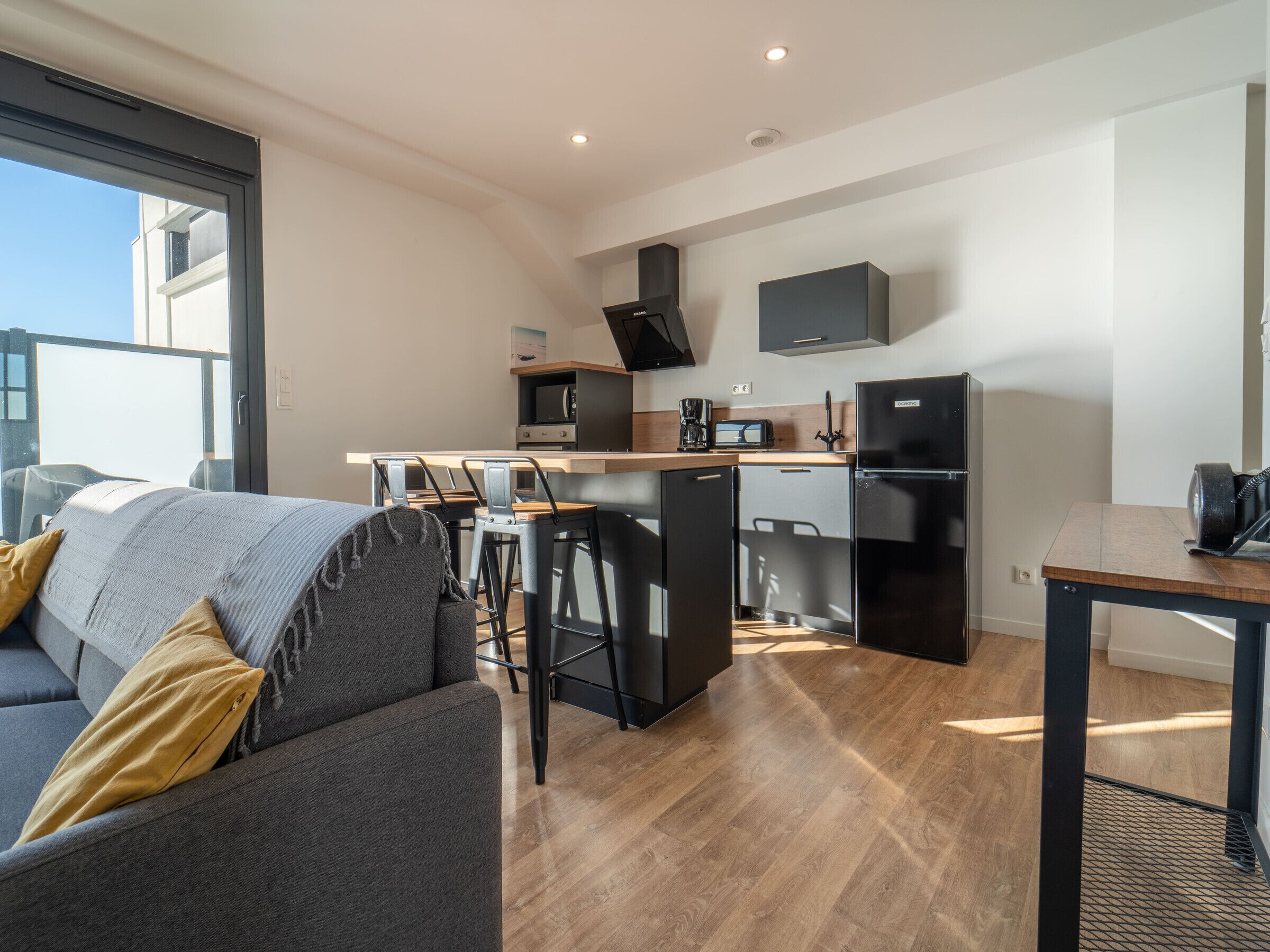 Eine moderne Wohnung mit Wohnbereich, Küchenzeile und einem Balkon.