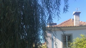 A courtyard with a stone pathway, a white wall, and a building with a tiled roof.