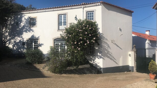 A two-story building with a white exterior, a tiled roof, and a gravel driveway.