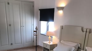 A bedroom with a green quilted bedspread, a bedside lamp, a nightstand, and a wardrobe.