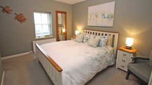 A bedroom with a large bed, bedside tables, a chair, a window, and a painting on the wall. - Findochty Beach House - Private Garden-beachfront (Buckie)