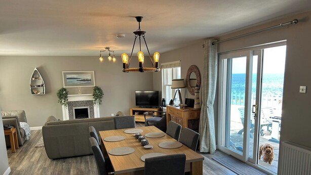 A modern living room with a dining area, a fireplace, and a large sliding glass door to the outside. - Findochty Beach House - Private Garden-beachfront (Buckie)