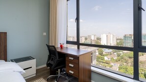 Une chambre à coucher avec un bureau en bois, une chaise, un lit et une grande fenêtre donnant sur la ville.