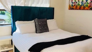 Una cama bien hecha con un cabecero color turquesa, ropa de cama blanca y una manta negra.