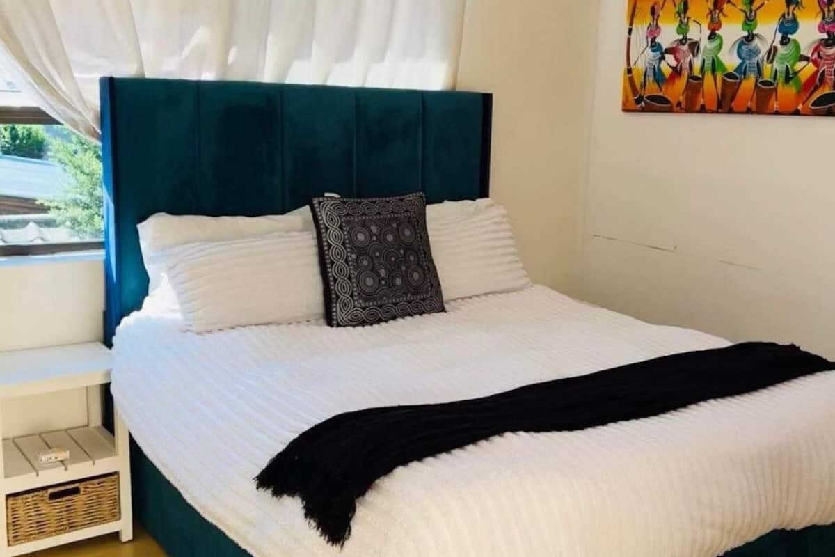 A neatly made bed with a teal headboard, white bedding, and a black throw blanket.