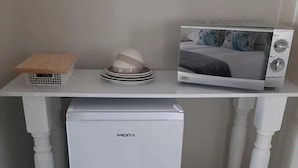Una kitchenette compacta con un refrigerador blanco, microondas y un pequeño bote de basura.