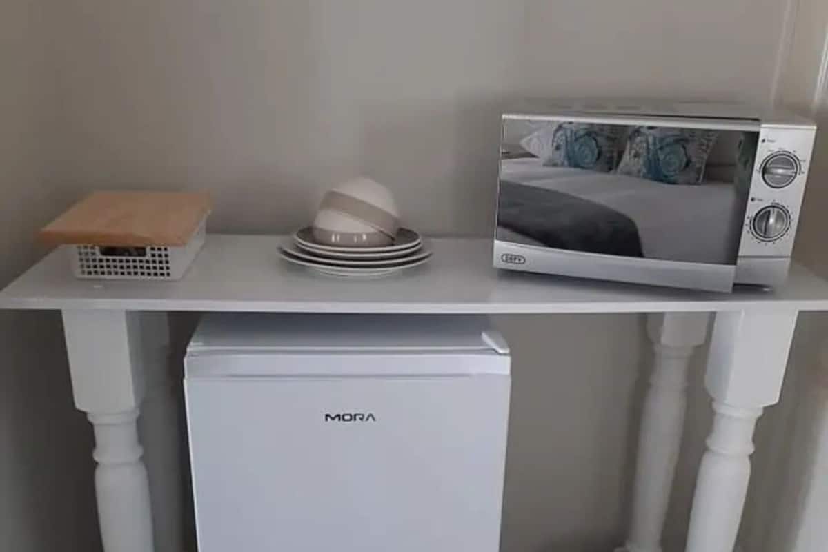 A compact kitchenette with a white refrigerator, microwave, and a small trash bin.