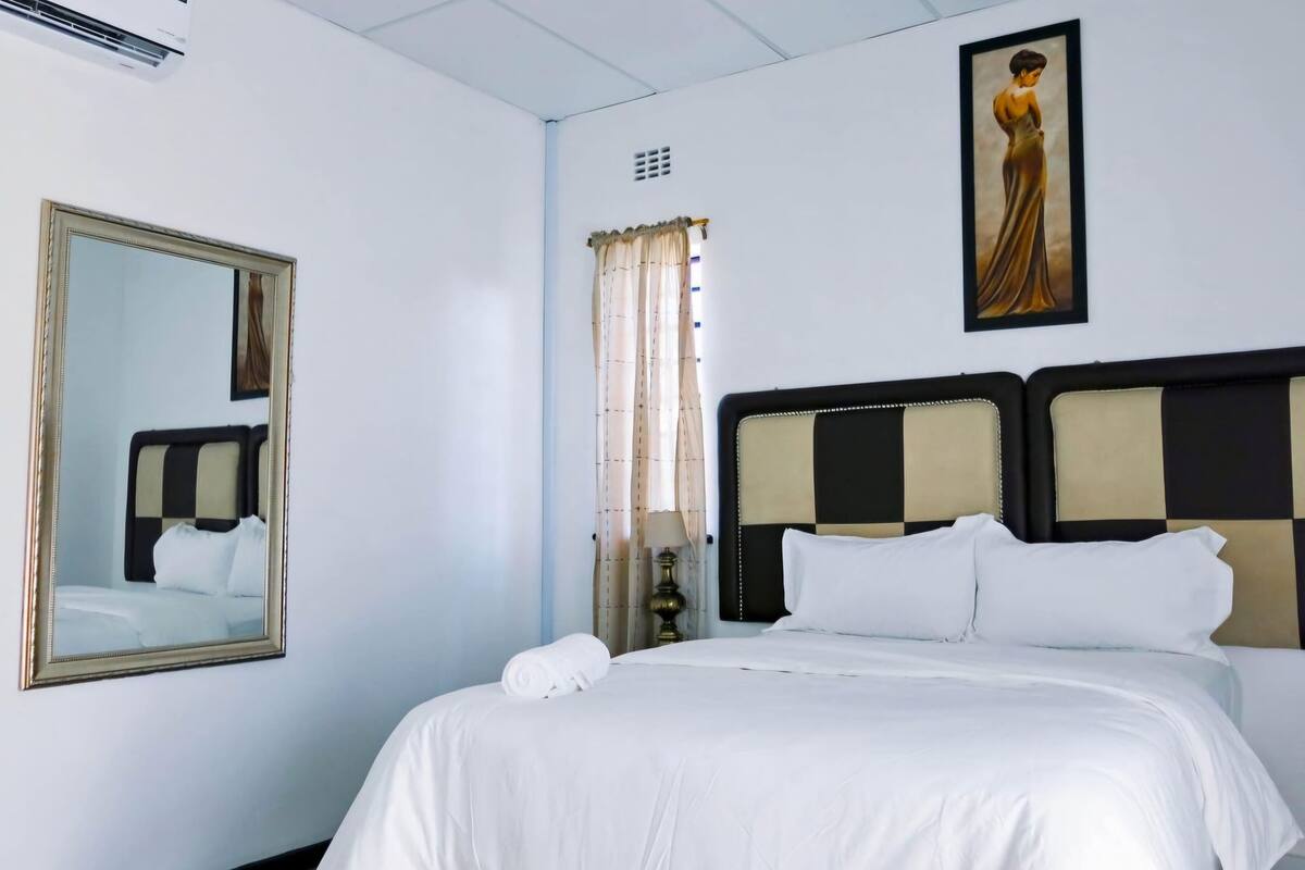 A hotel room with a large bed, a mirror, a painting, and an air conditioning unit.