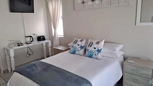 Una habitación de hotel con una cama, mesita de noche y televisión montada en la pared.
