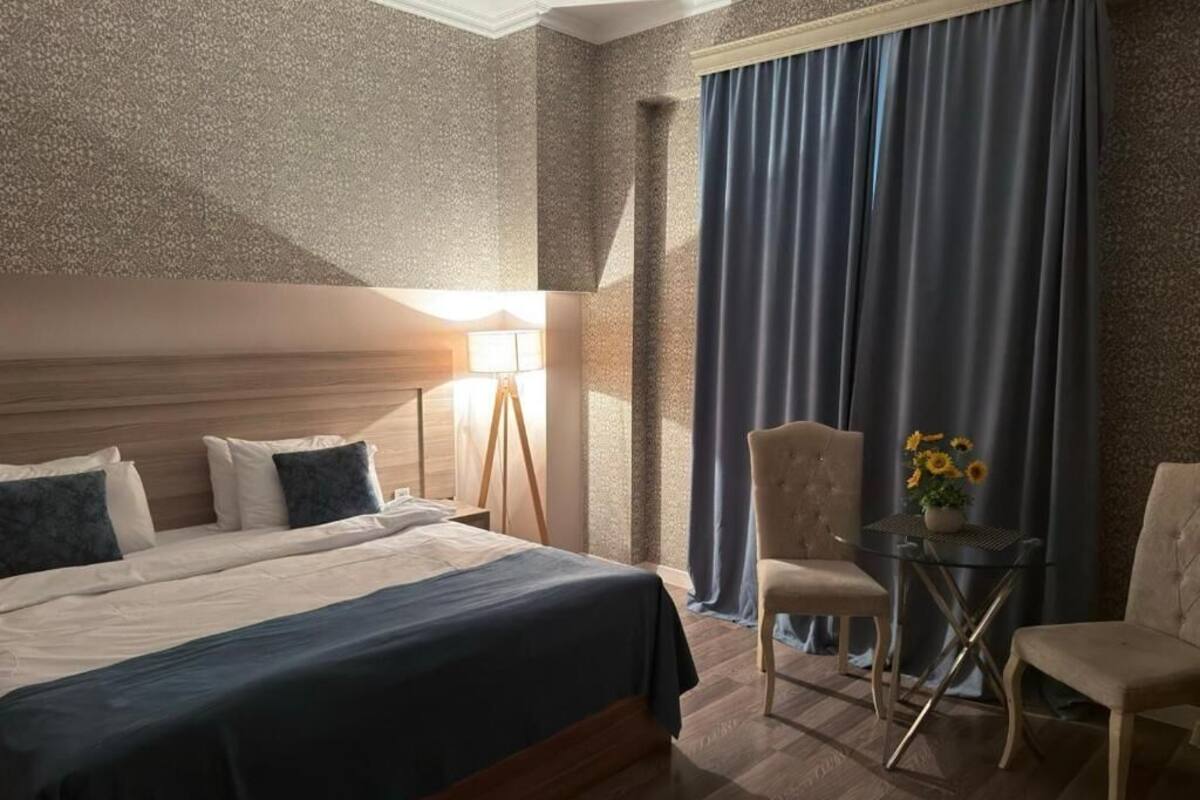 Une chambre d’hôtel avec un grand lit, un bureau avec une chaise, une lampe et une vue sur l’extérieur par une fenêtre munie de rideaux.