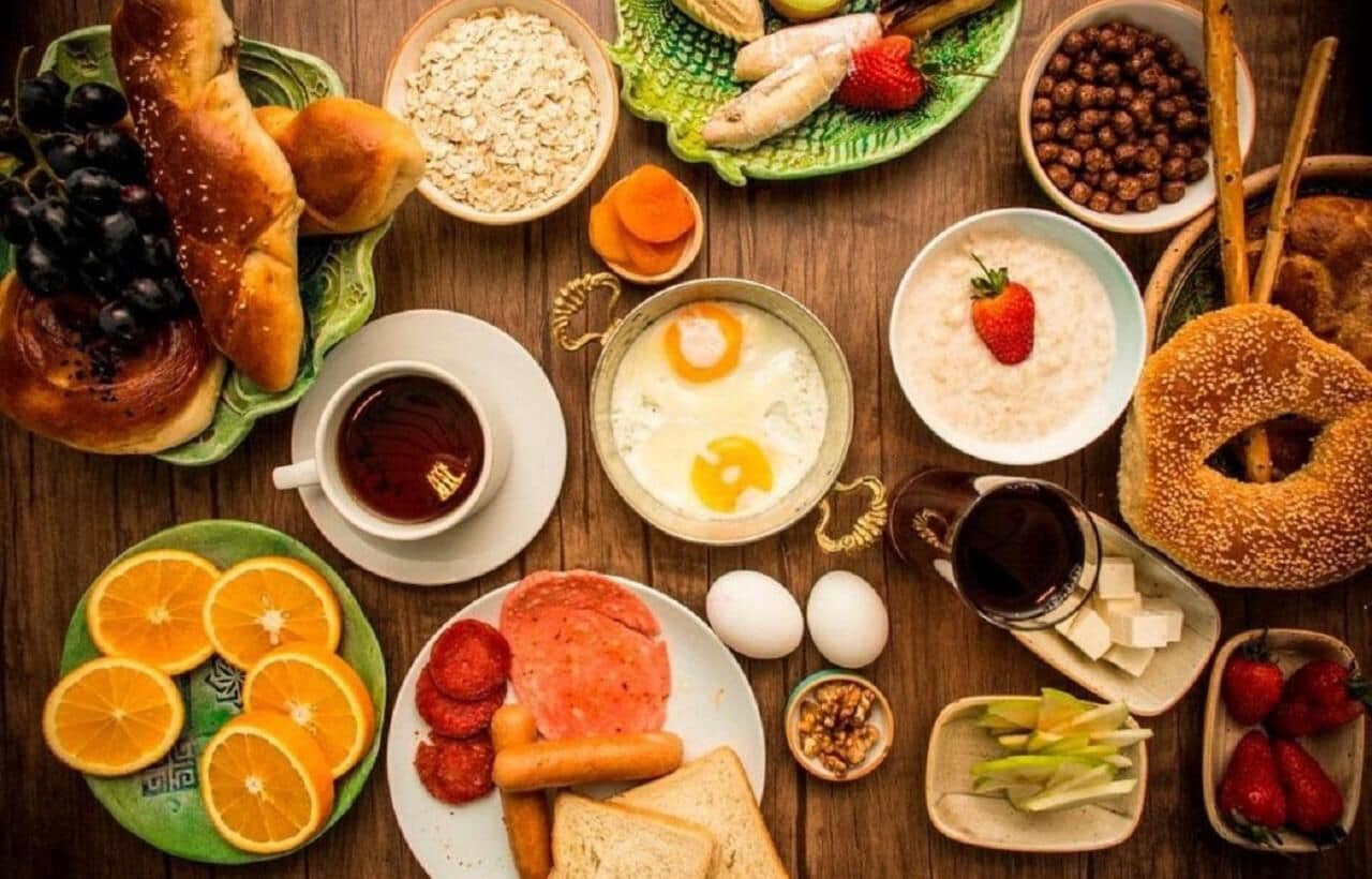 A variety of breakfast foods including bread, eggs, fruits, and beverages on a wooden table.