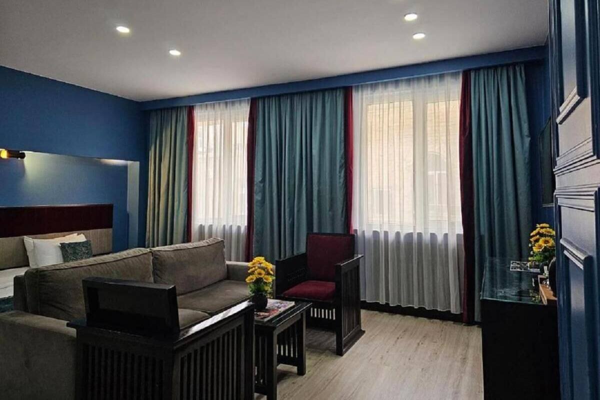 Une chambre d’hôtel moderne, dotée d’un canapé, d’un fauteuil et d’une petite table sur laquelle est posé un vase de fleurs.