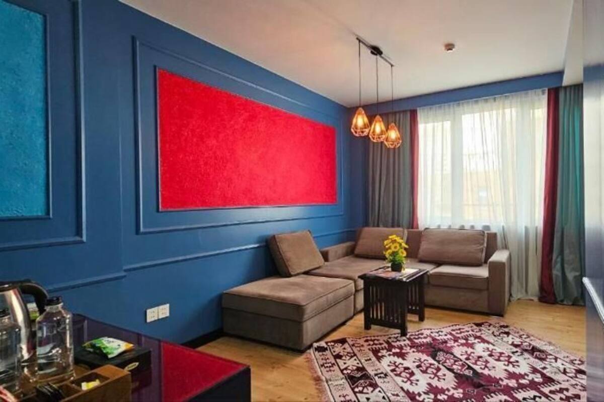 Un salon moderne avec un mur bleu, un mur d’accent rouge, un ensemble de canapés marron, une table basse et un tapis à motifs.