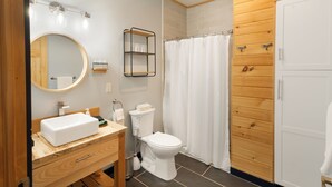 Ein modernes Badezimmer mit einem Holzbadezimmermöbel, einem runden Spiegel, einer Toilette und einer Duschvorhang.