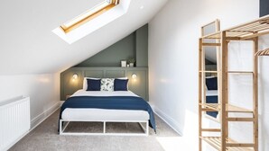 Un dormitorio con techo inclinado, una cama con estructura blanca, una escalera de madera y un tragaluz.