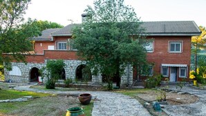 Una casa a due piani in mattoni con facciata in pietra, un cortile lastricato e un grande albero al centro.