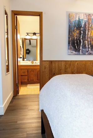 A bedroom with a wooden headboard, a white bedspread, and a painting of trees on the wall. - Buena Vista Garden Studio Apartment: STR-043 (Buena Vista)