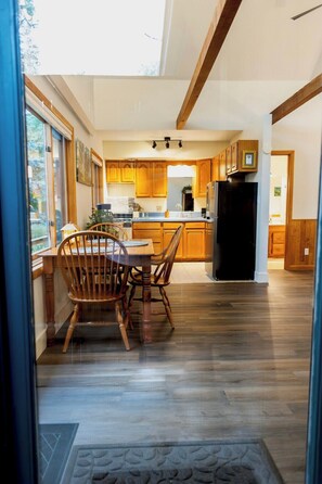 A modern kitchen with wooden cabinets, a dining table with chairs, and a large window providing natural light.