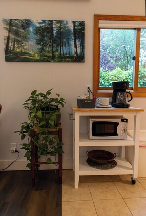 Eine Küchenzeile mit einer weißen Mikrowelle, einer Kaffeemaschine und einem Blumentopf auf einem Holzboden.