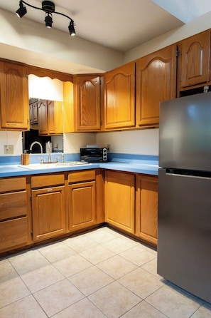 A kitchen with wooden cabinets, a stainless steel refrigerator, a microwave, and a sink. - Buena Vista Garden Studio Apartment: STR-043 (Buena Vista)