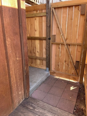 A wooden gate with a metal latch, a concrete step leading up to it, and a paved area with bricks. - Buena Vista Garden Studio Apartment: STR-043 (Buena Vista)