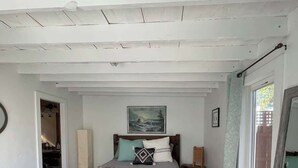 Un dormitorio con cama, un cuadro sobre la cama, una ventana con cortinas y suelo de madera.