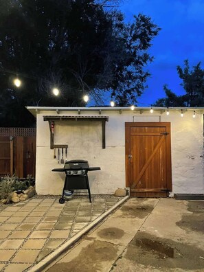 A backyard with a barbecue grill, a wooden door, and a string of lights.