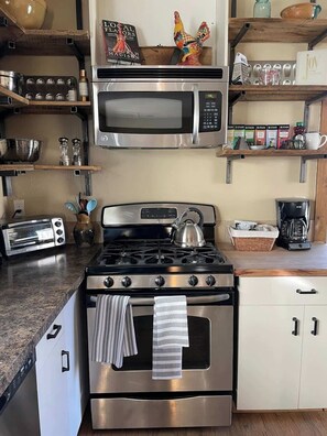 Una cocina con estufa, microondas, tostadora y varios utensilios de cocina en estantes.