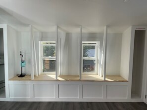 A room with a built-in bench with windows, a fire extinguisher on the wall, and a lamp on the bench.