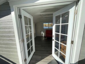 A hallway with a door leading to a room with a red chair and a window.